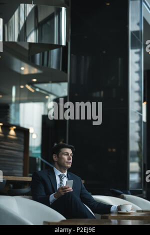 Thoughtful businessman using mobile phone while having coffee Stock Photo
