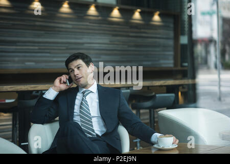 Businessman talking on phone while having coffee Stock Photo