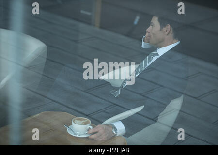 Businessman talking on mobile phone while having coffee Stock Photo