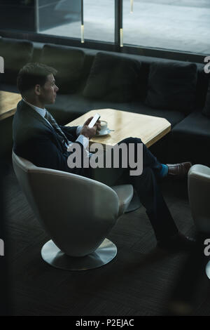Thoughtful businessman using mobile phone while having coffee Stock Photo