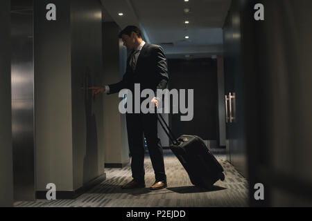 Businessman with trolley bag waiting for lift Stock Photo