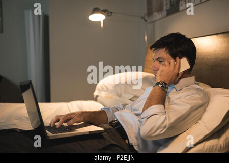 Businessman using laptop while talking on mobile phone Stock Photo
