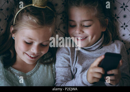 Siblings using mobile phone on bed Stock Photo