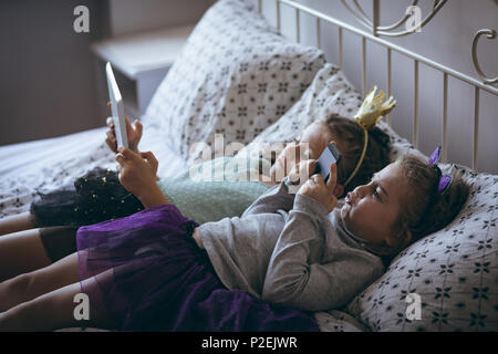 Siblings using mobile phone and digital tablet on bed Stock Photo