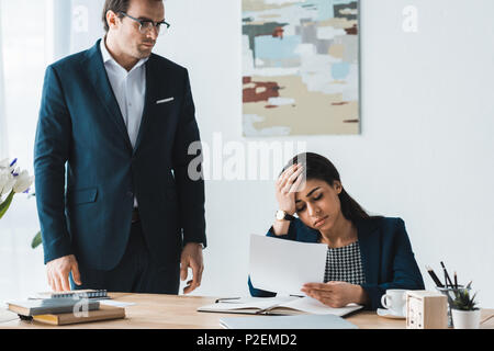 Businessman looking at stressed businesswoman with papers in hands Stock Photo