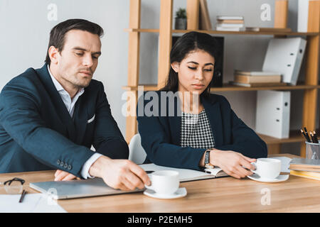 Male and female colleagues drinking coffee at workplace Stock Photo