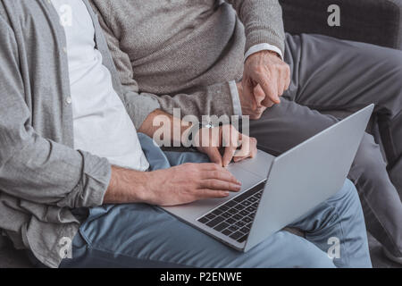 cropped image of adult son and senior father using laptop together at home Stock Photo