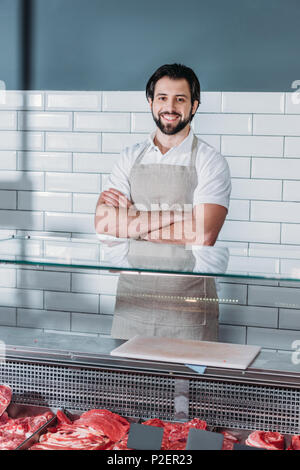 portrait of smiling shop assistant in apron with arms crossed standing at counter in supermarket Stock Photo