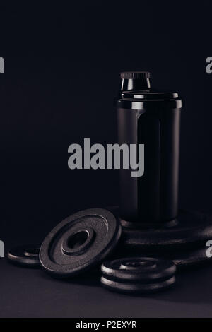 black protein shaker on pile of weight plates isolated on black Stock Photo