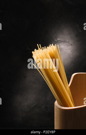 bunch of raw spaghetti in wooden container with garlic on black surface Stock Photo