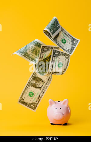 Dollar banknotes falling into pink piggy bank with glasses on white ...