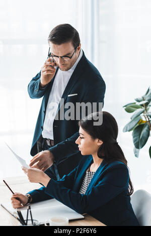 Businessman talking on phone and looking at papers in businesswoman hands Stock Photo