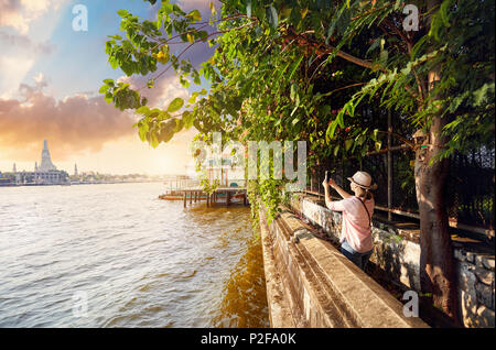 Woman tourist taking a picture of Wat Arun with her phone at sunset in Bangkok, Thailand Stock Photo