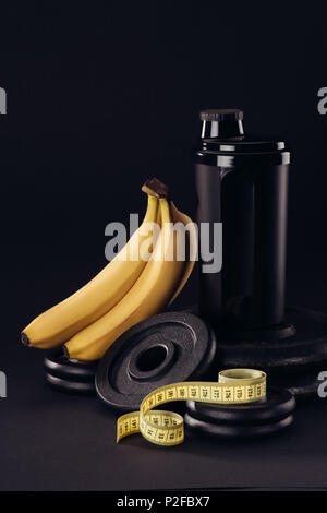 black protein shaker on pile of weight plates with bananas and measuring tape isolated on black Stock Photo