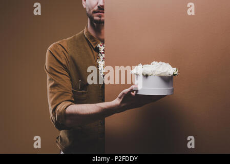 Young man in vintage styled clothes holding box with flowers isolated on brown Stock Photo