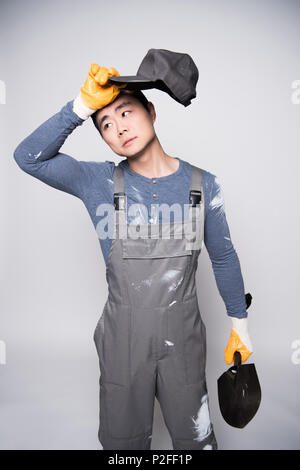 Young construction worker in overalls and safety gloves wiping the sweat from his forehead. Stock Photo