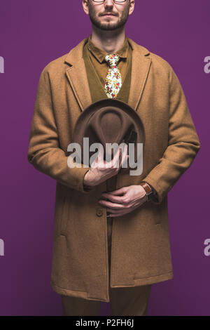 Stylish man in coat with hat in hands isolated on purple Stock Photo