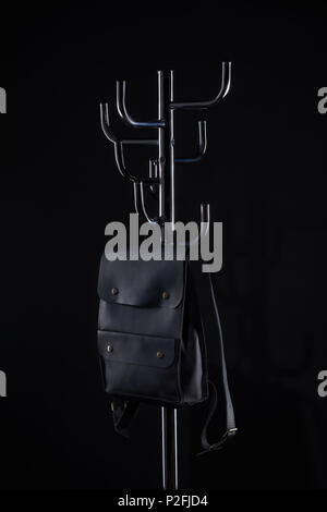 black leather backpack hanging on coat rack isolated on black Stock Photo