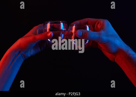 cropped shot of man and woman clinking glasses under toned light isolated on black Stock Photo