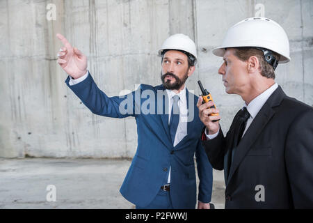 Professional architects in hardhats using walkie-talkie and discussing project at construction site Stock Photo