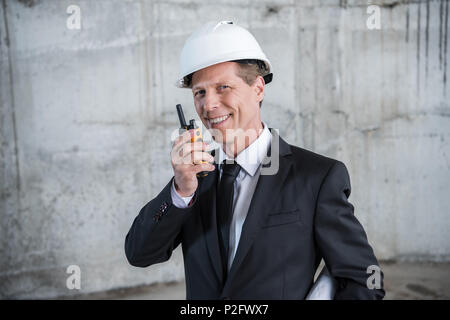 Professional mature architect using walkie-talkie and smiling at camera Stock Photo