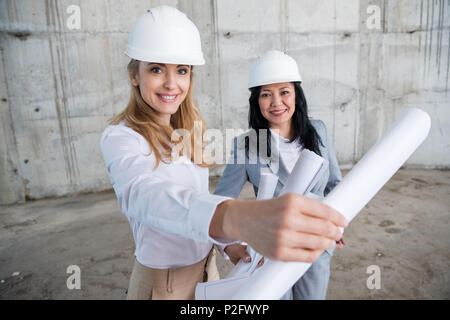 Two attractive smiling architects holding blueprint while working at construction site Stock Photo