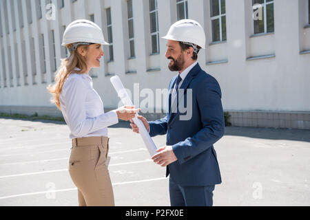 Professional middle aged architects in helmets holding blueprint and discussing project Stock Photo