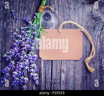 Lavender flowers (Lavandula) with paper tag on an old wooden table. Art photo in purple tone. Stock Photo
