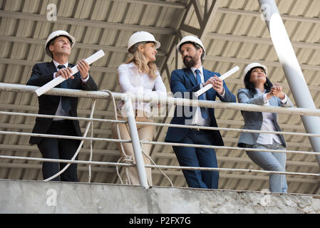 team of contractors in formal wear talking while standing at construction site Stock Photo