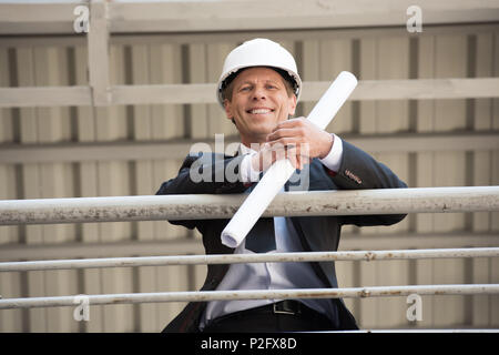 smiling middle aged architect in suit looking at camera and holding blueprint Stock Photo