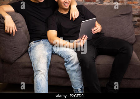 Gay couple watching and looking at phone tablet together. Portrait of happy gay men - Homosexual love concept Stock Photo