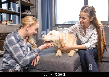 two girls hugging golden retriever dog on sofa at home, teenagers having fun concept Stock Photo