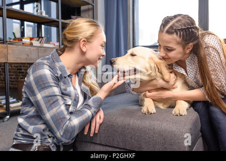 two girls hugging golden retriever dog on sofa at home, teenagers having fun concept Stock Photo