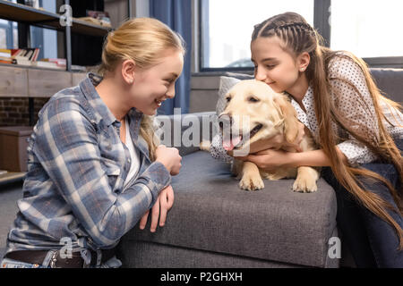 two girls hugging golden retriever dog on sofa at home, teenagers having fun concept Stock Photo