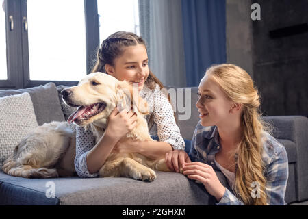 two girls hugging golden retriever dog on sofa at home, teenagers having fun concept Stock Photo