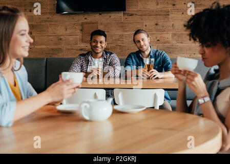 Two young men having beer and looking at women sitting at next table in cafe Stock Photo