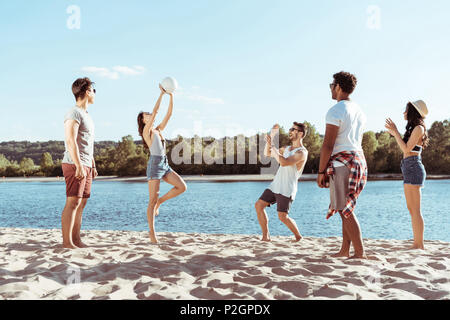 happy young friends playing volleyball on sandy beach at daytime Stock Photo