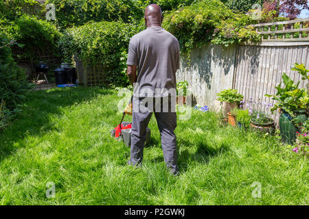 A black man mowing long grass in the backyard garden lawn at home Stock Photo