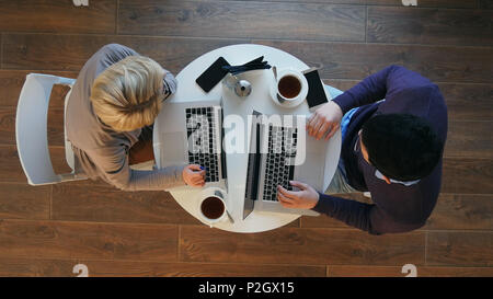 Young successful business couple is discussing documents, drinking coffee and smiling while working in cafe Stock Photo