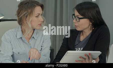 Two female colleagues brainstorming in the office using tablet Stock Photo