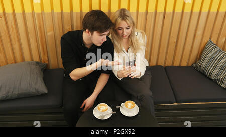 Happy couple using smartphone together and drinking coffee in cafe Stock Photo
