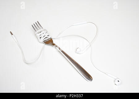 the headphones wrapped up a fork on a white surface Stock Photo