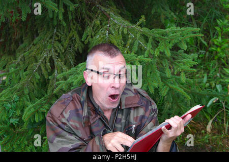 Surprised man reading operating manual or book sitting under a fir tree Stock Photo