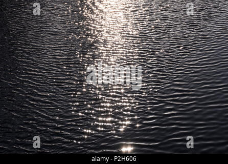 Sunlight twinkling and reflecting on black canal water ripples Stock Photo