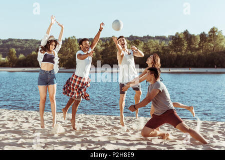 young smiling friends playing beach volleyball on riverside at daytime Stock Photo