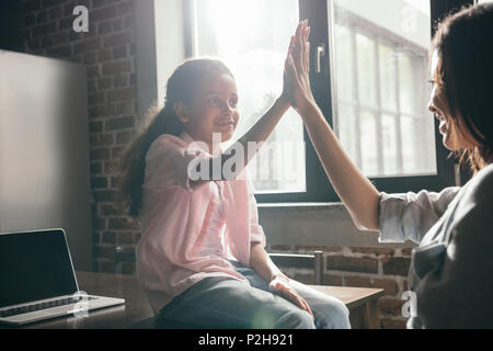 african american daugher giving high five to her mother while sitting on table at home Stock Photo