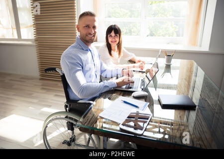 Portrait Of Smiling Disabled Businessman With His Colleague Working On Laptop Stock Photo