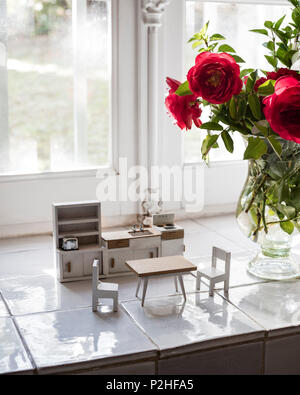 Dolls house furniture and red roses on windowsill in 18th century Luberon farmhouse. Stock Photo