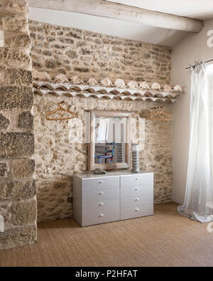 Empty clothes hangers with wooden mirror on chest of drawers in 18th century Luberon farmhouse. Stock Photo