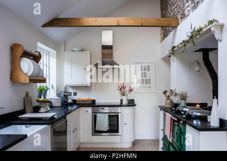Modernised country kitchen featuring original flint wall, Howdens kitchen units and matt black granite worktops. The wooden plate rack is from Haus Stock Photo